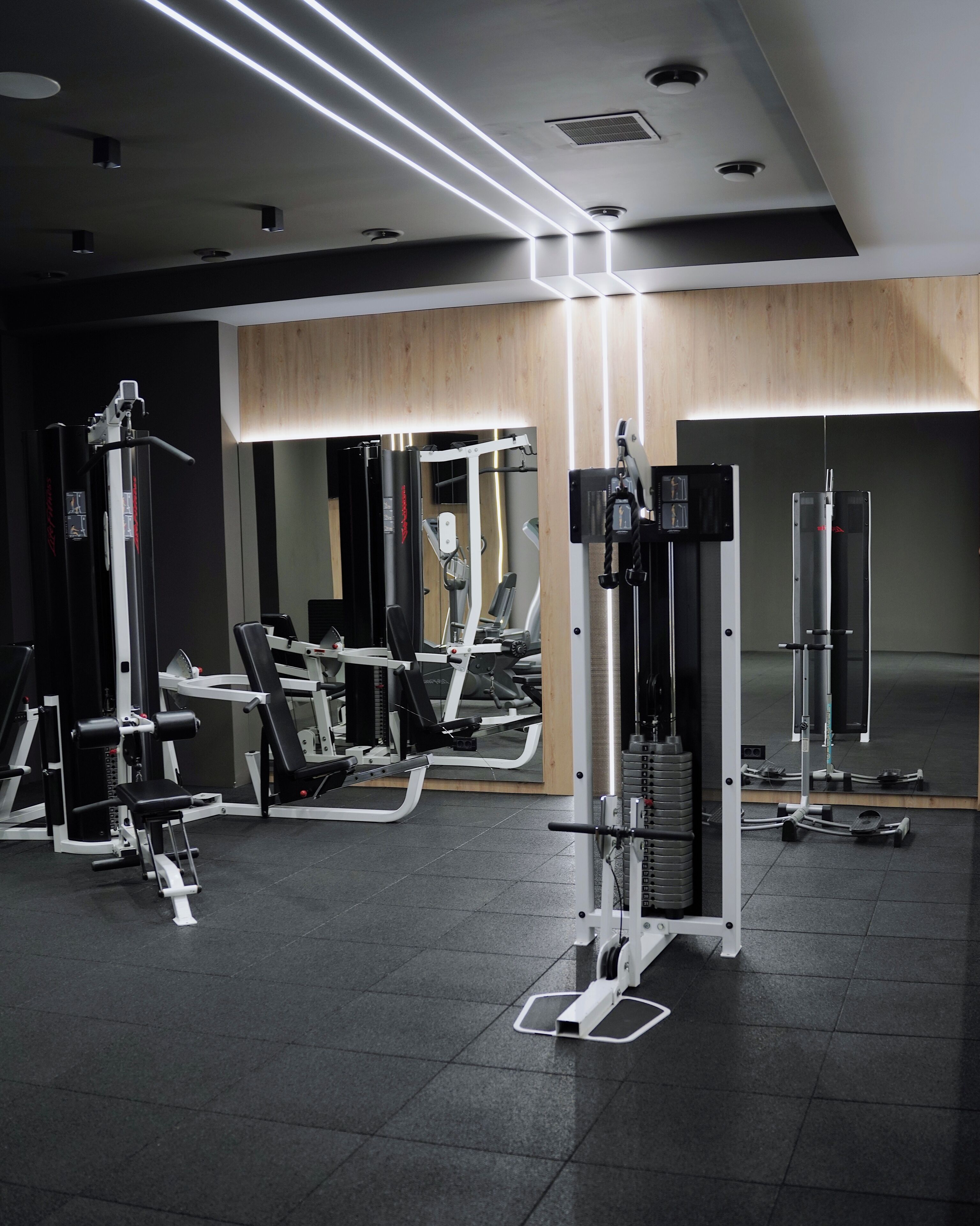 A modern gym with various exercise machines, a mirror, and a wooden accent wall.