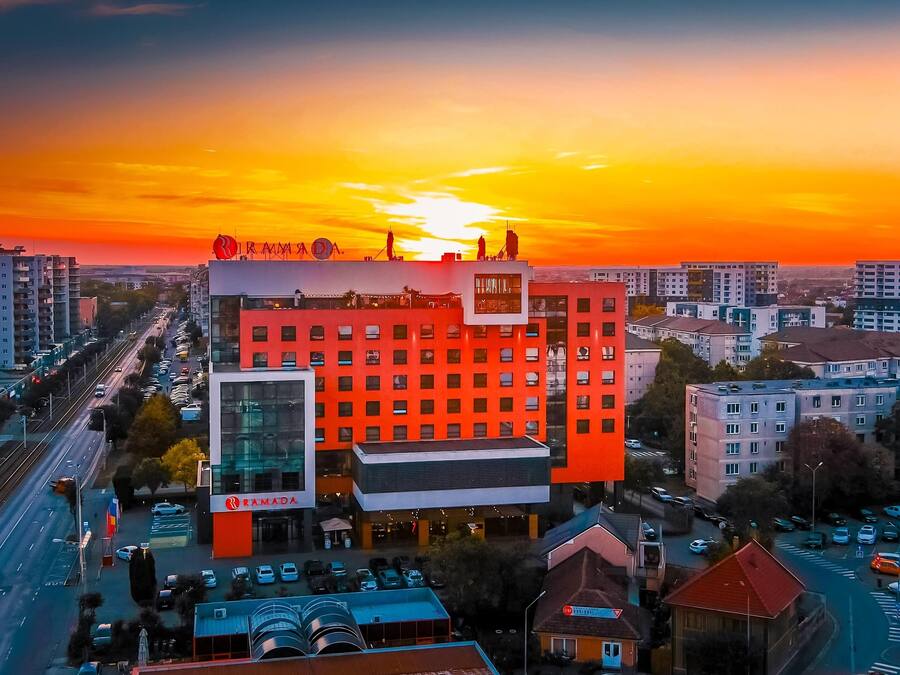 Un hotel de varios pisos con una llamativa fachada roja, ventanas amplias y una terraza en la azotea.