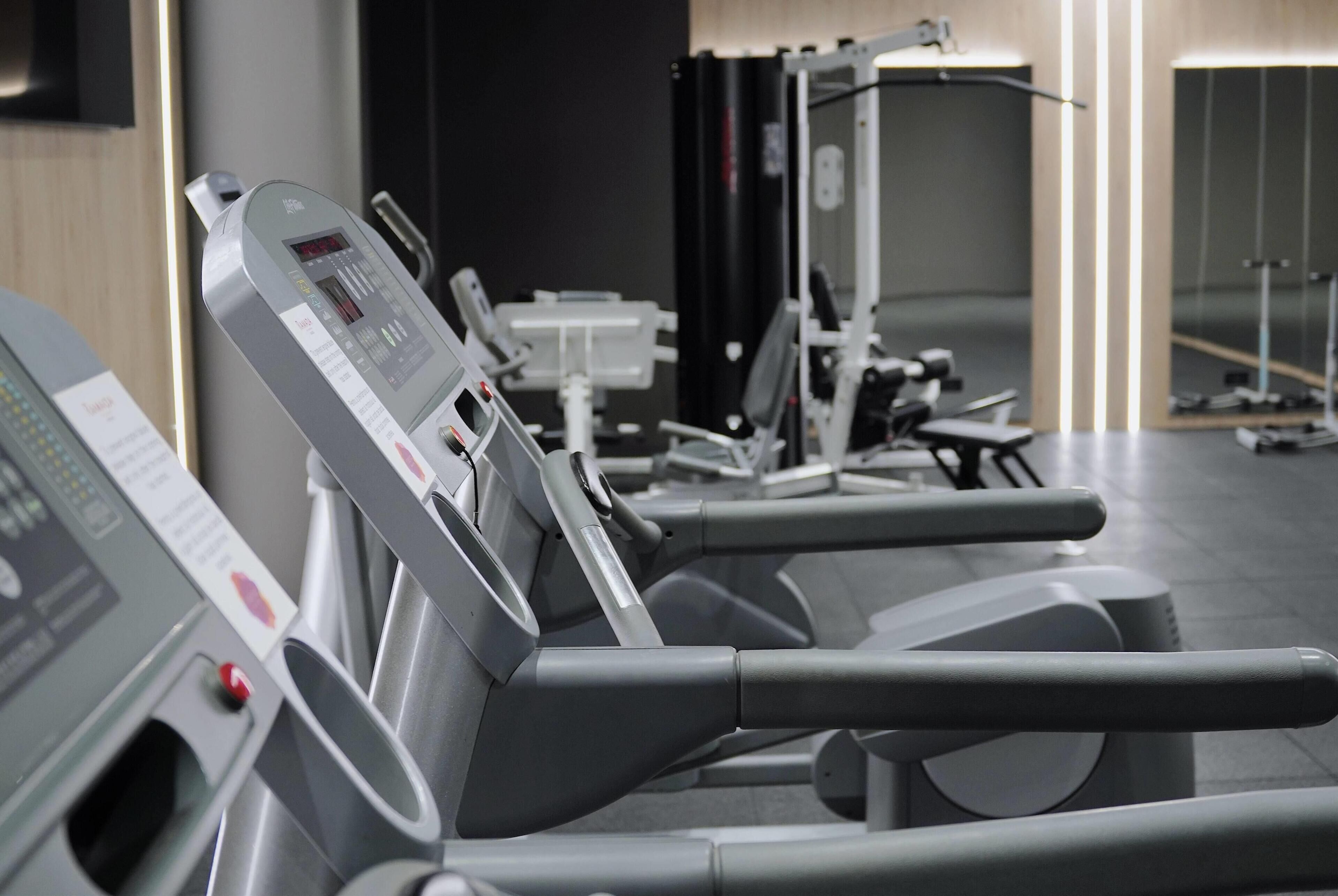 Varias bicicletas estáticas alineadas en un gimnasio, cada una con pantalla digital y panel de control.