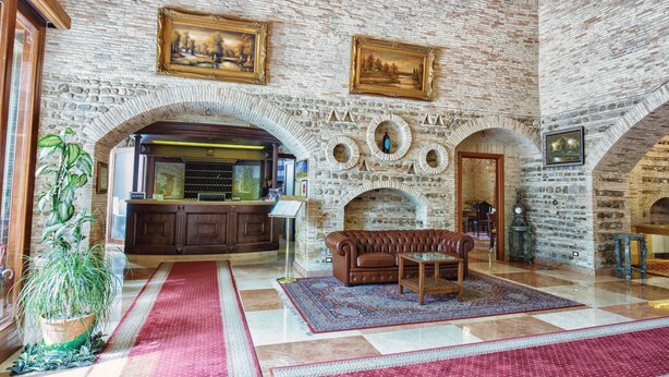 A spacious lobby with a stone wall, a reception desk, a fireplace, and a leather sofa. - Grand Hotel Vigna Nocelli (Lucera)