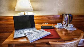 Una scrivania in legno con un portatile, un giornale, una lampada, una caffettiera e una tazza e un piattino.