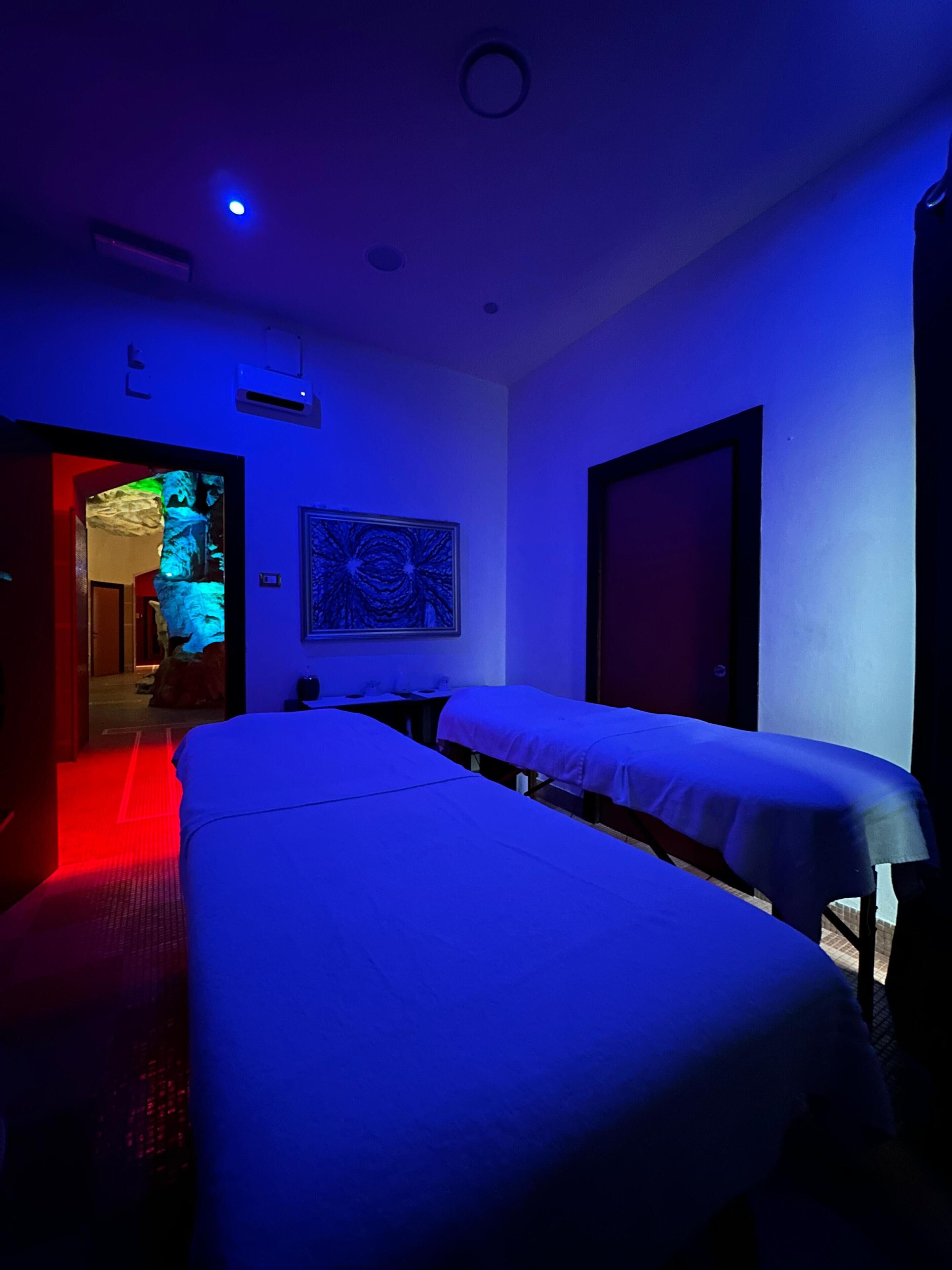 A room with two massage tables, a wall-mounted air conditioner, and a door leading to another room.