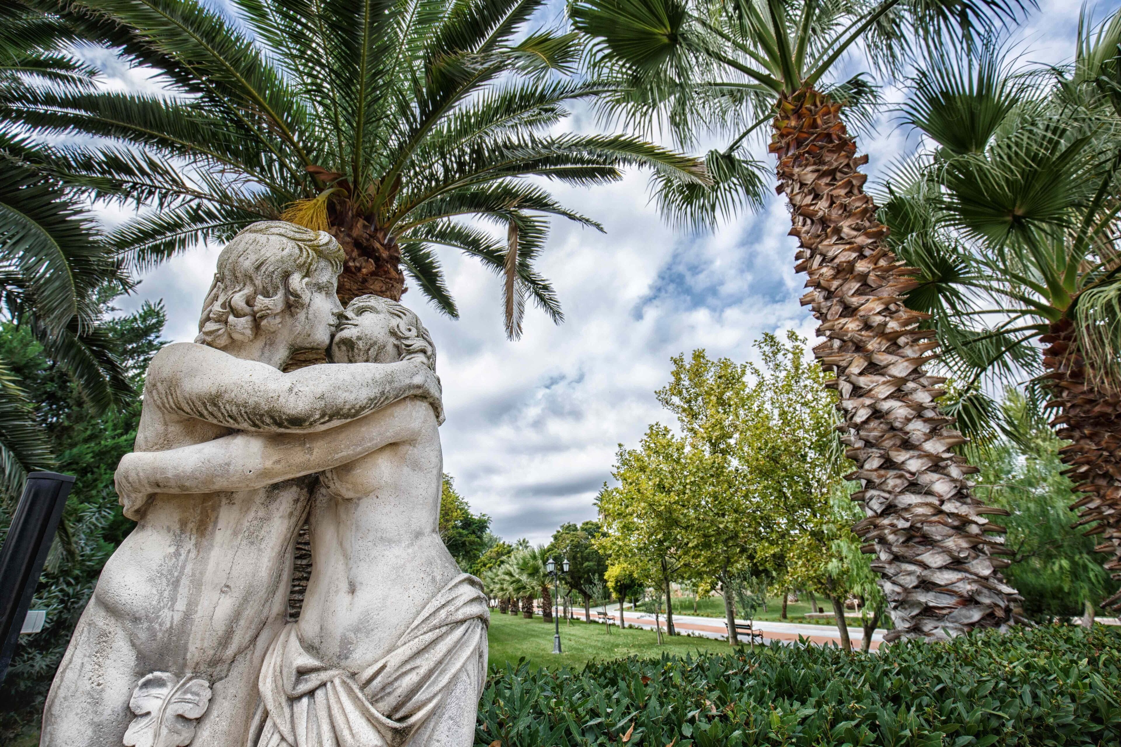 A statue of a man embracing a woman, surrounded by palm trees and greenery.