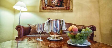 Una mesa de comedor con una jarra, un cuenco de fruta y dos copas de vino.