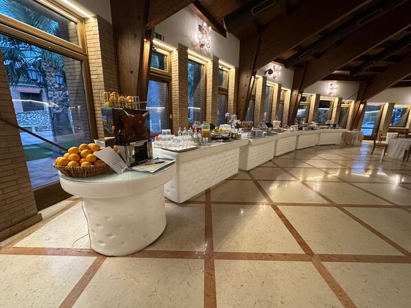 Disposición de bufé con estación de café, cesta de frutas y diversas opciones de comida y bebida.