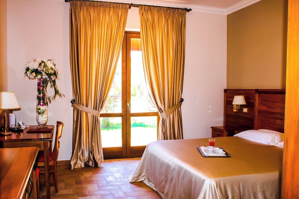 A hotel room with a bed, a desk, a chair, a nightstand, a lamp, and a window with curtains.