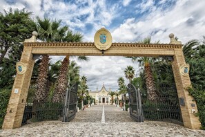 A grand entrance with a stone archway, palm trees, and a building in the background. - Grand Hotel Vigna Nocelli (Lucera)