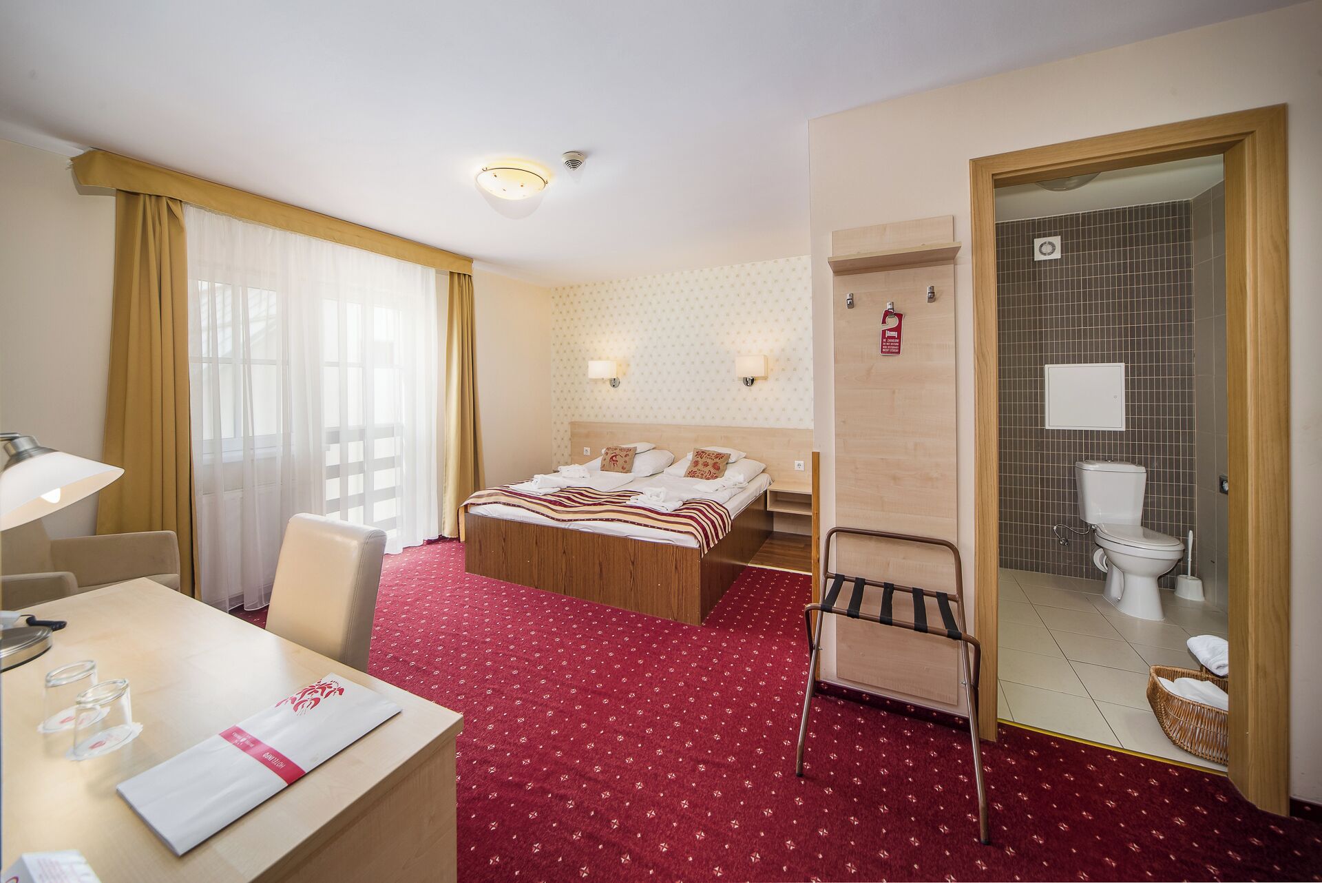 A hotel room with a bed, a desk, a chair, a bathroom with a toilet and a mirror.