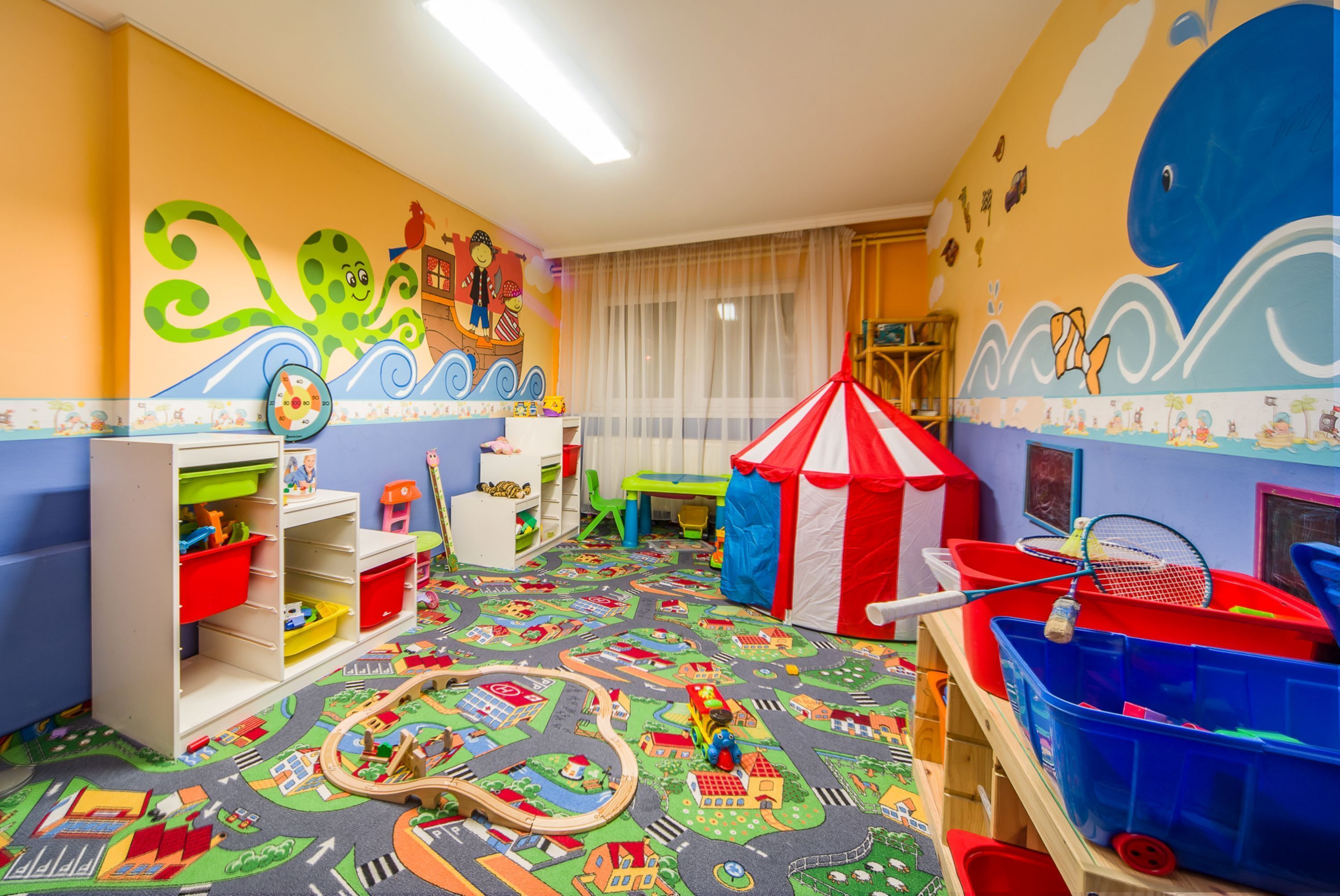 Een kinderspeelruimte met een kleurrijk vloerkleed, een speelgebied en een tent.