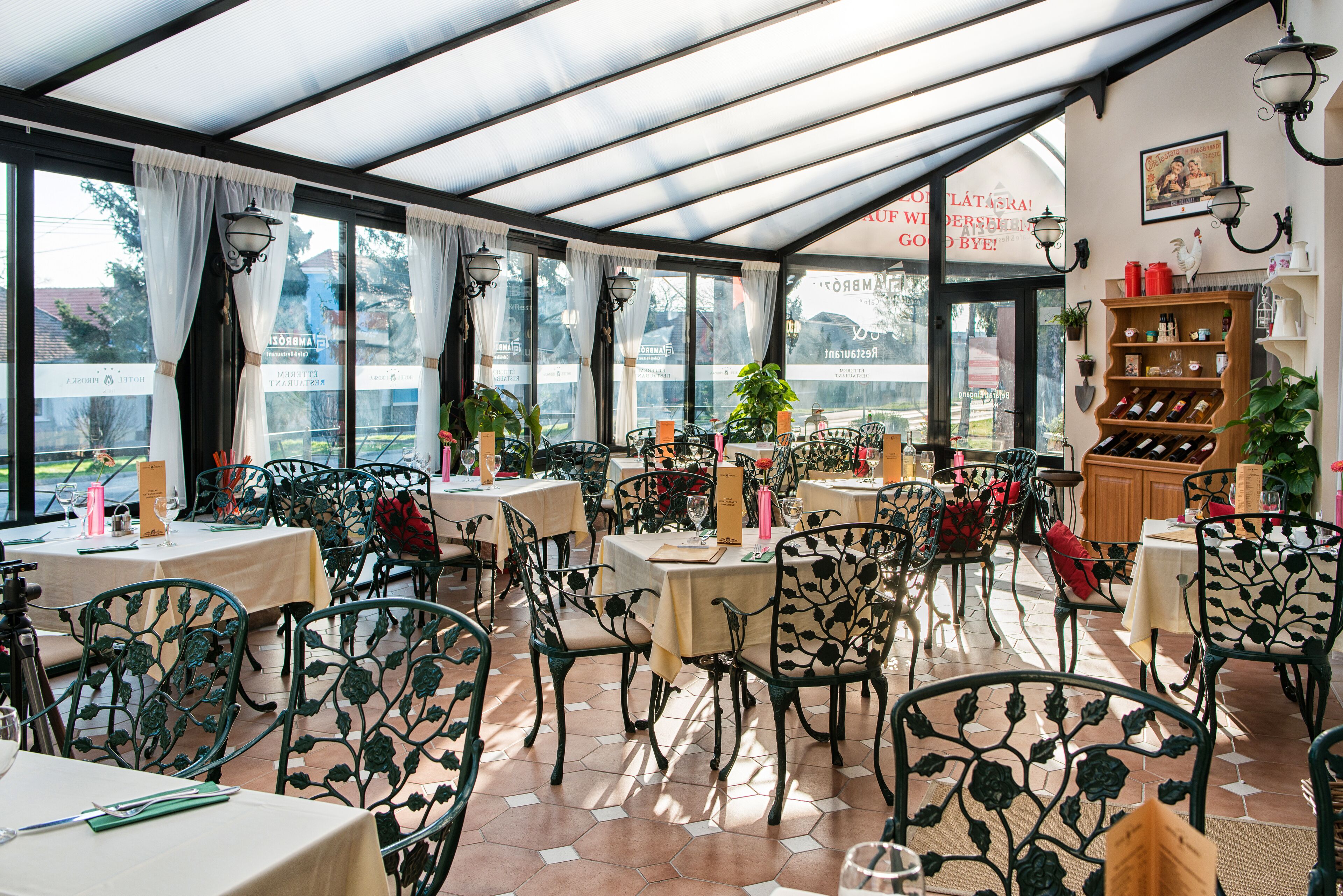 A restaurant with outdoor seating under a glass roof, featuring metal chairs and tables with menus.