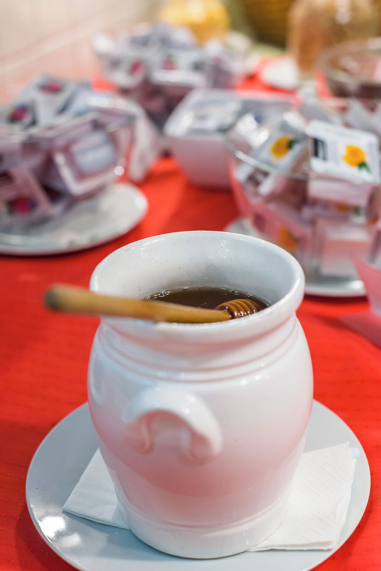 Une tasse en céramique blanche, dotée d’une anse, contenant un liquide foncé et un petit récipient pour le miel, posée sur une soucoupe blanche avec une serviette en dessous.