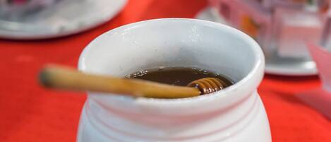 Une tasse en céramique blanche, dotée d’une anse, contenant un liquide foncé et un petit récipient pour le miel, posée sur une soucoupe blanche avec une serviette en dessous.