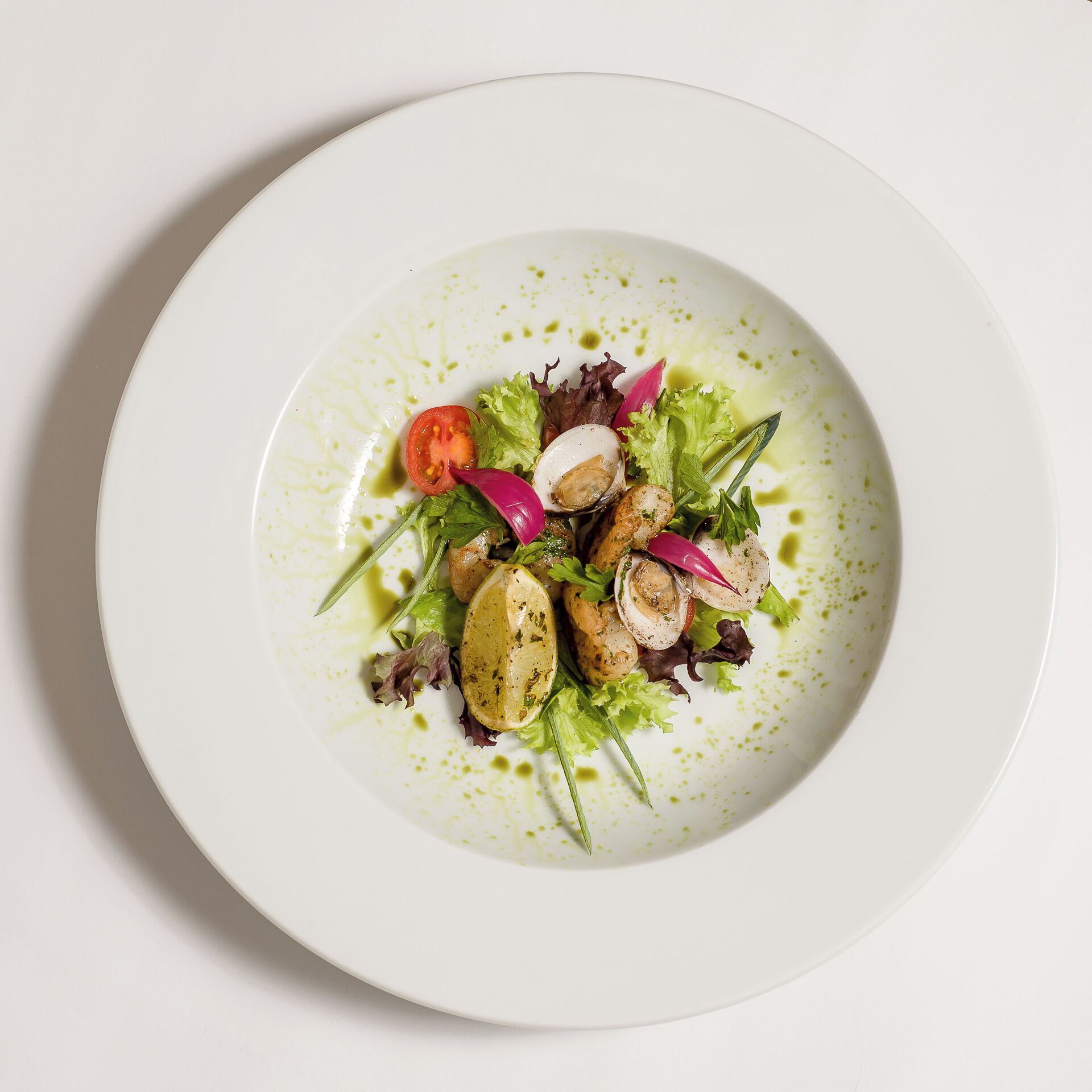 A white plate with a salad consisting of greens, a tomato slice, radish, and possibly chicken or tofu, garnished with herbs.