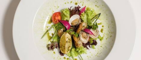 A white plate with a salad consisting of greens, a tomato slice, radish, and possibly chicken or tofu, garnished with herbs.