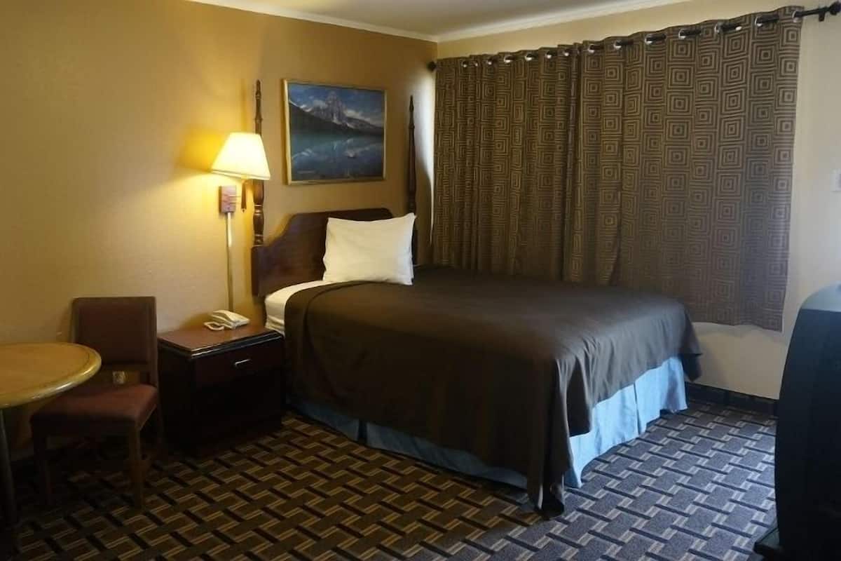 A hotel room with a bed, a desk with a lamp, a chair, and a small table.