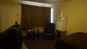 A hotel room with a bed, a chair, a small table, a microwave, and a door. - Budget Inn Malvern (Malvern)