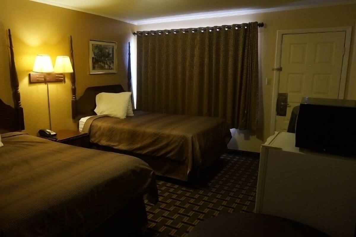 A hotel room with two beds, a desk, a lamp, a television, and a door.