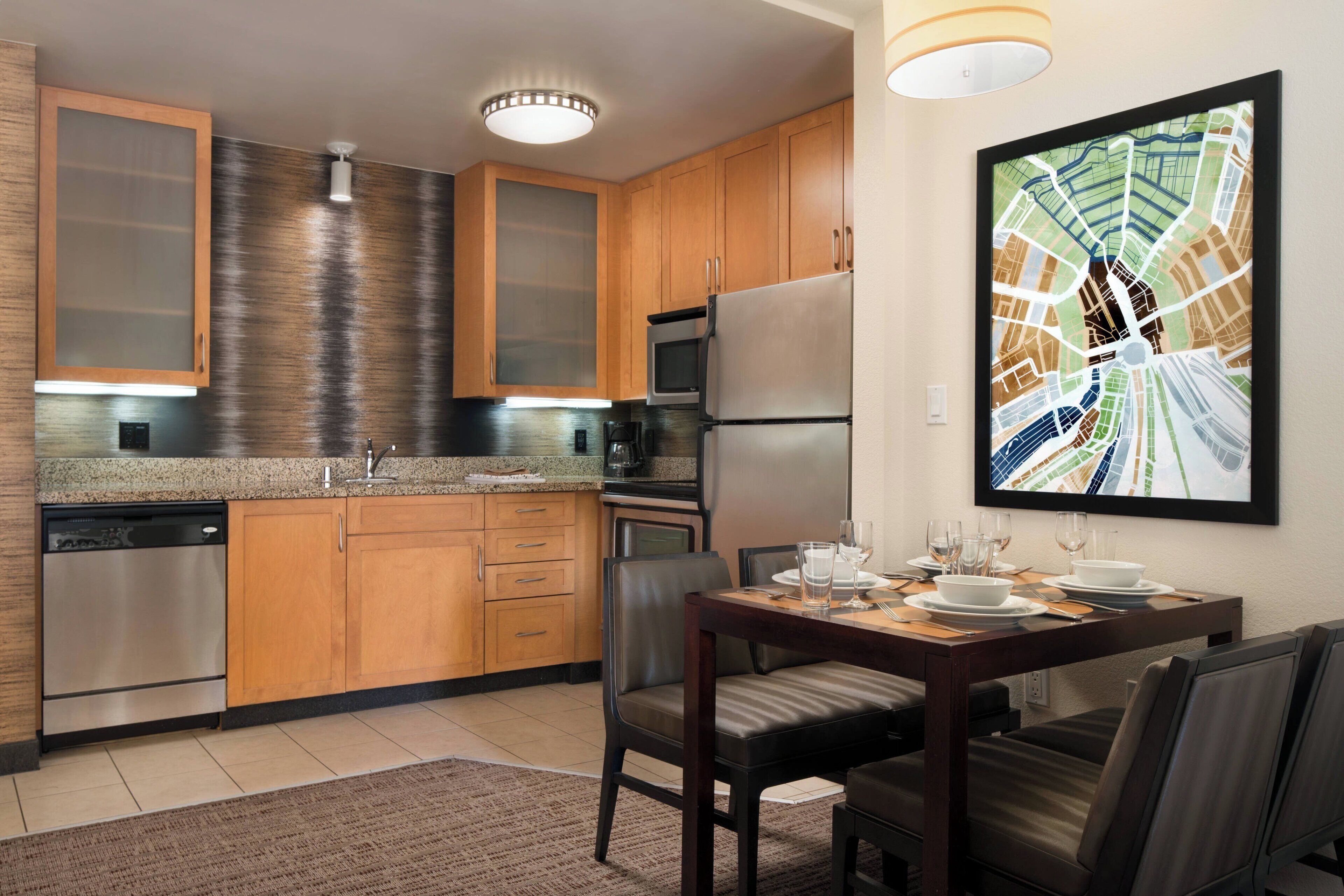 A modern kitchen with wooden cabinets, stainless steel appliances, and a dining area with a table set for four.