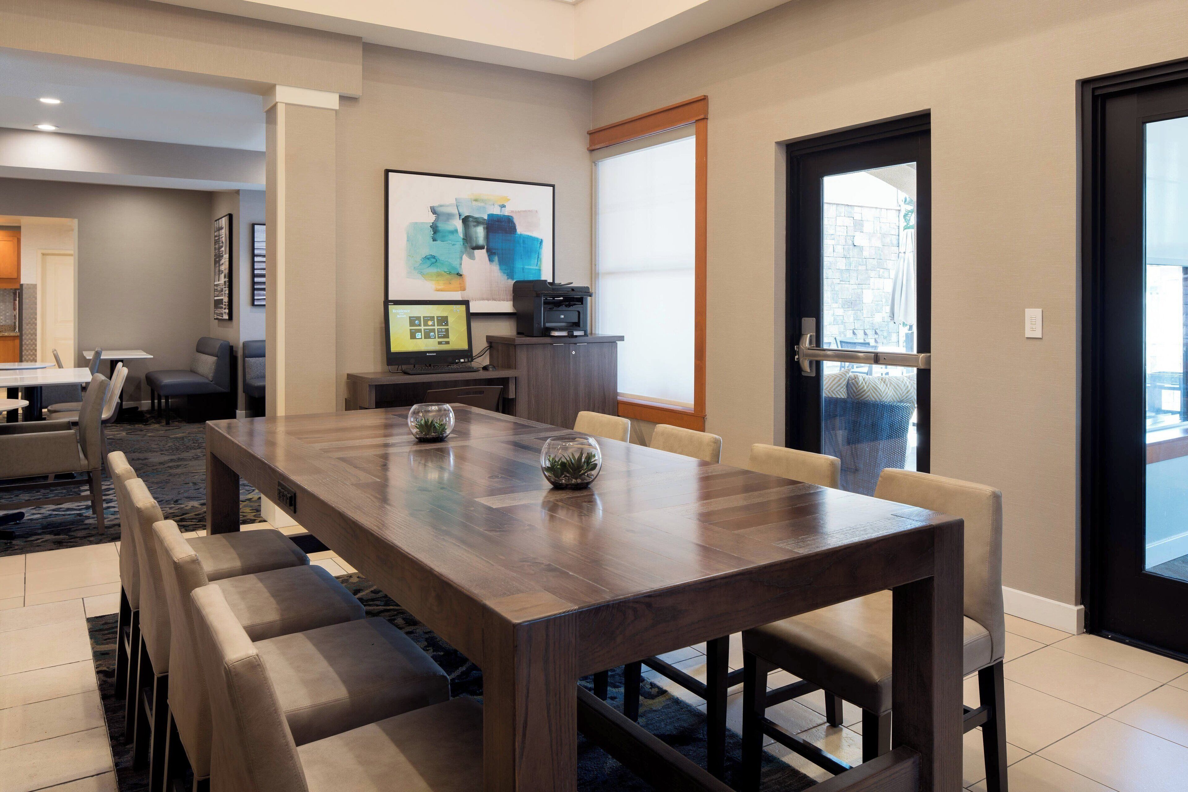 A modern dining area with a wooden table, cushioned chairs, and a projector screen.
