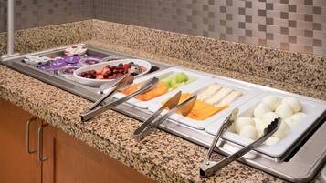 Buffet com diversas opções de comida, incluindo frutas, legumes e ovos.