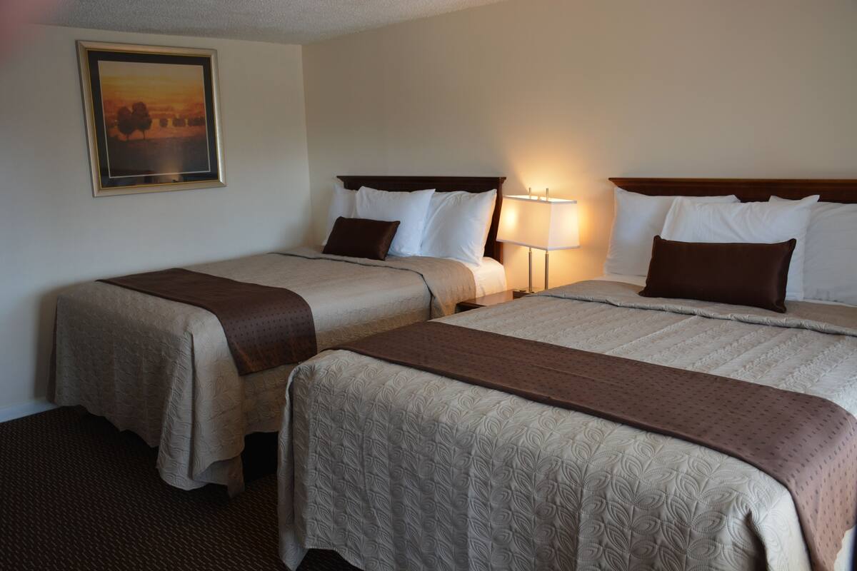 A hotel room with two beds, a nightstand, a lamp, and a framed picture on the wall.