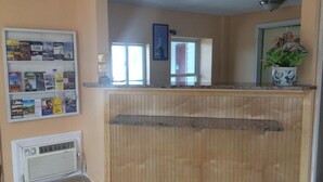 A reception area with a wooden counter, a bulletin board with various notices, a potted plant, and a door leading to another room. - Liberty Inn (Old Saybrook)