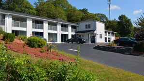 A motel with a two-story structure, a covered parking area, and a landscaped front yard with various plants. - Liberty Inn (Old Saybrook)