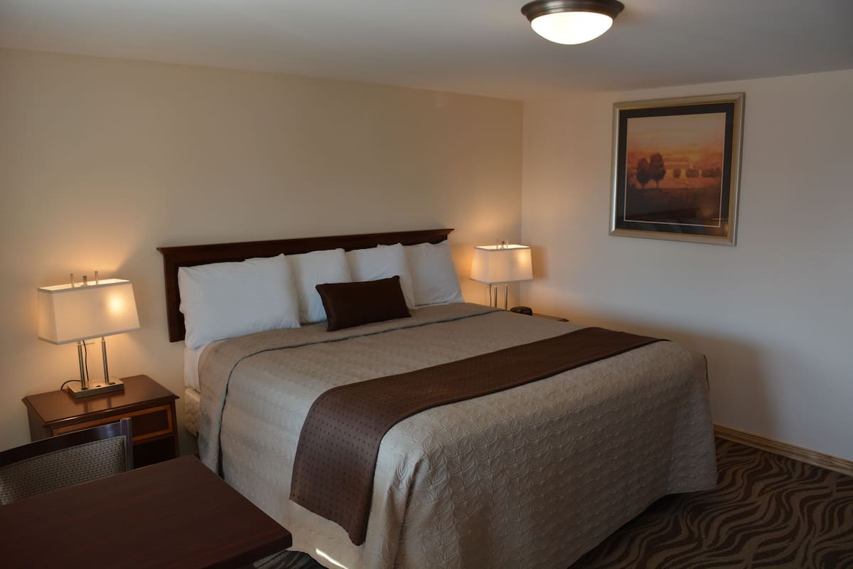 A hotel room with a large bed, two bedside tables with lamps, a chair, and a framed picture on the wall.