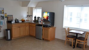 A kitchen with wooden cabinets, a refrigerator, a coffee maker, and a fruit bowl. - Liberty Inn (Old Saybrook)