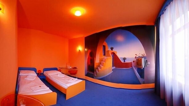 A room with two beds, a small table, and a view of a coastal landscape through a large window. - Hotel Liberec (Liberec)