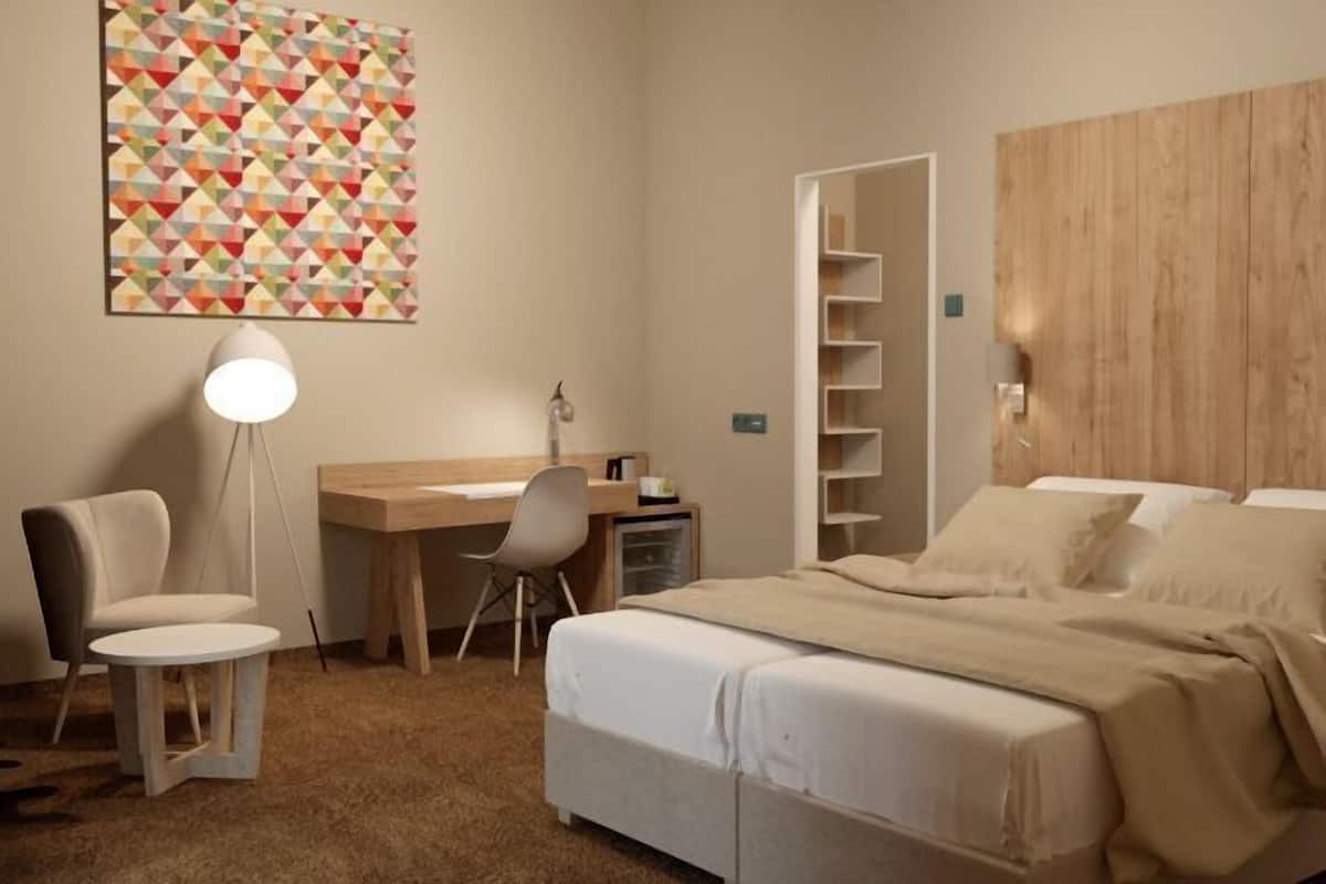 A bedroom with a bed, a desk, a chair, a lamp, and a wall art piece.