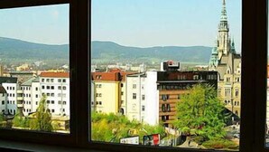 A view through a window of a cityscape with a prominent church spire, residential buildings, and a mountain range in the background. - Hotel Liberec (Liberec)