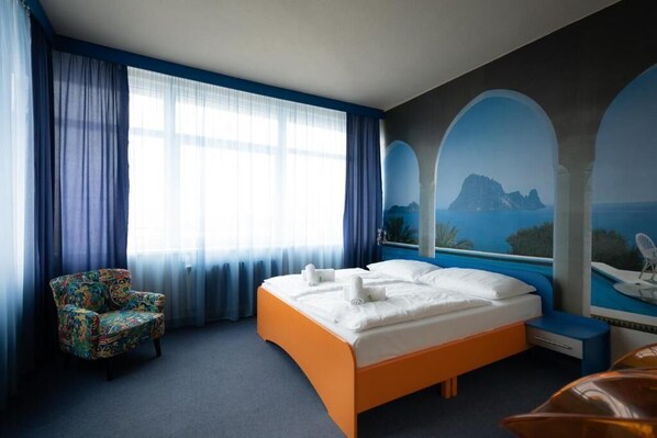 A hotel room with a bed, a chair, and a large window with curtains.