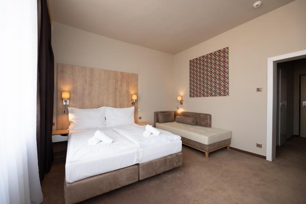 A hotel room with a large bed, a smaller sofa bed, and a wall-mounted artwork.