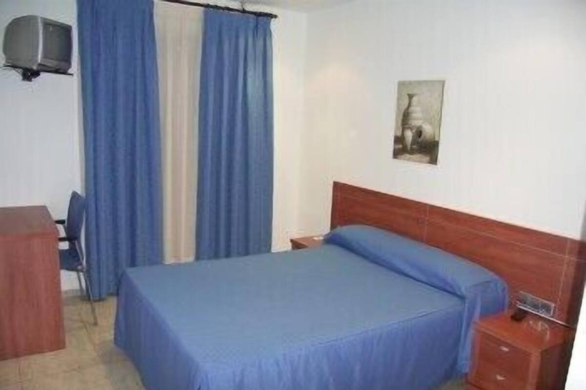 A bedroom with a bed, a desk, a chair, a TV, and curtains.