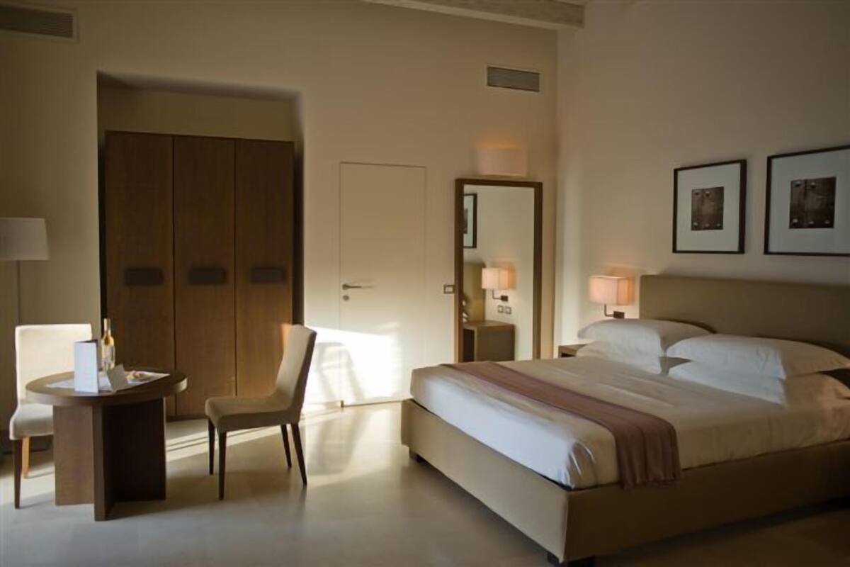 A hotel room with a bed, a chair, a desk, a wardrobe, and two framed pictures on the wall.