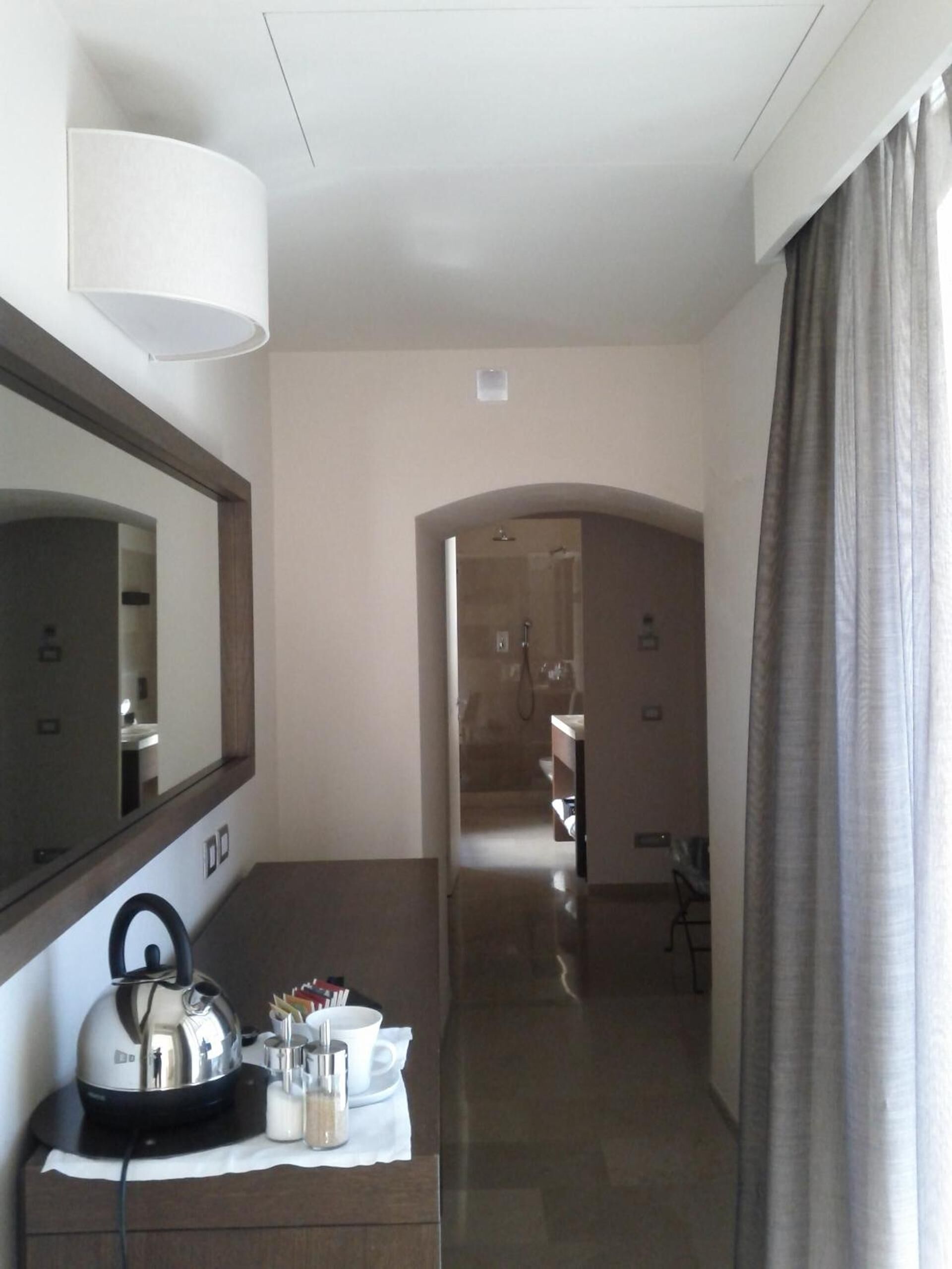 A hotel hallway with a mirror, a kettle, and a tray with cups and condiments.
