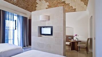 Habitación de hotel con dos camas, un televisor instalado en una pared de piedra, un escritorio con una silla y una mesita con un florero.