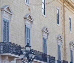 A building with multiple windows, some with shutters, and a balcony with ornate metal railings and a street lamp. - Marè Resort (Trani)