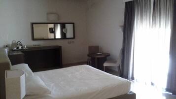 Une chambre d’hôtel avec un lit, un bureau, une chaise, une petite table et une grande fenêtre avec des rideaux.