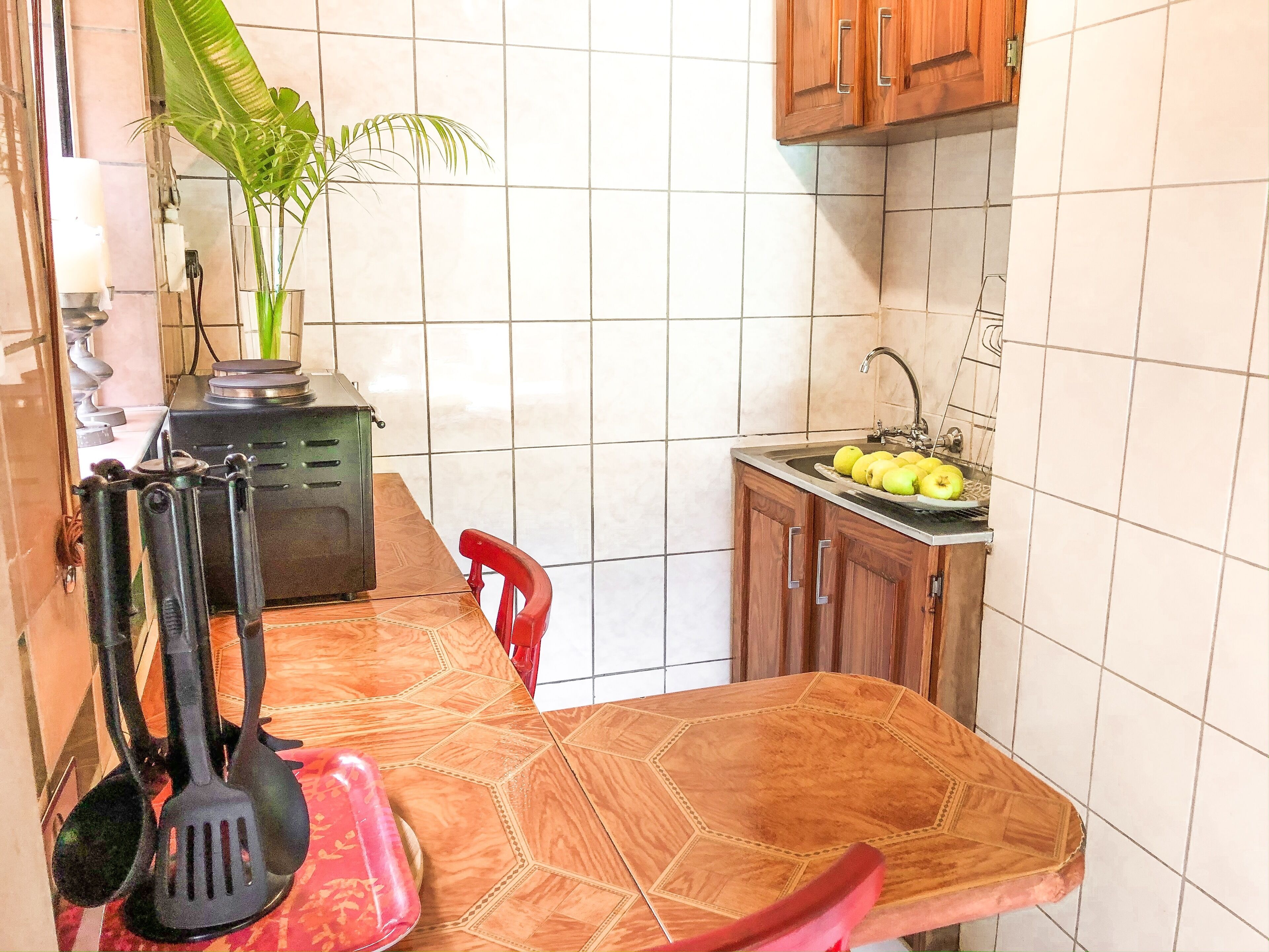 A kitchen with a wooden table, a red chair, a sink with apples, and a plant.