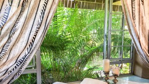 A room with a large window, curtains, a cushioned bench, and a candle holder. - Ingwenya Lodge (St. Lucia)