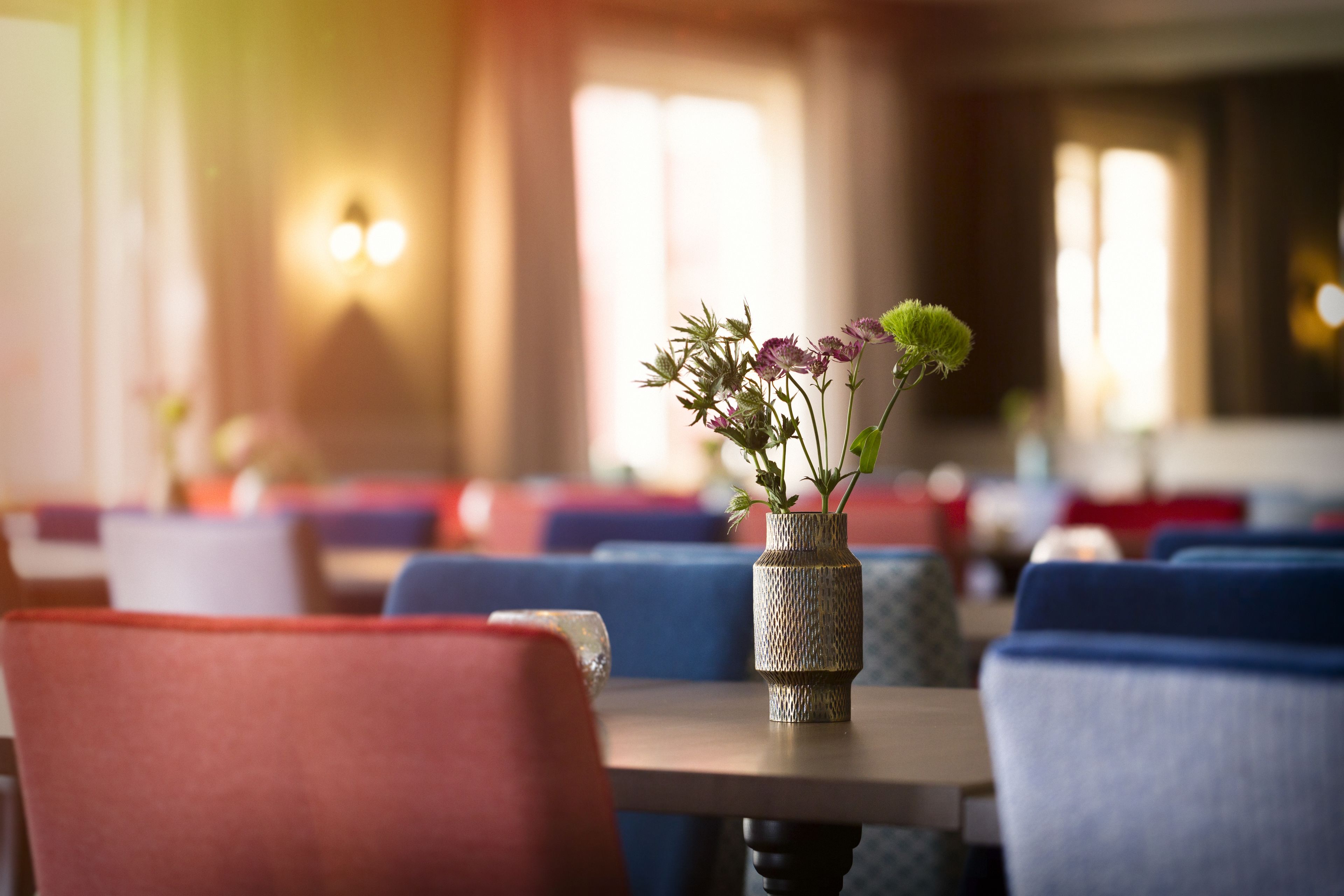 A dining area with tables and chairs, a vase with flowers, and a wall-mounted light fixture.
