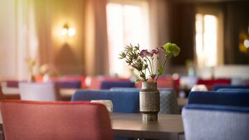 A dining area with tables and chairs, a vase with flowers, and a wall-mounted light fixture.