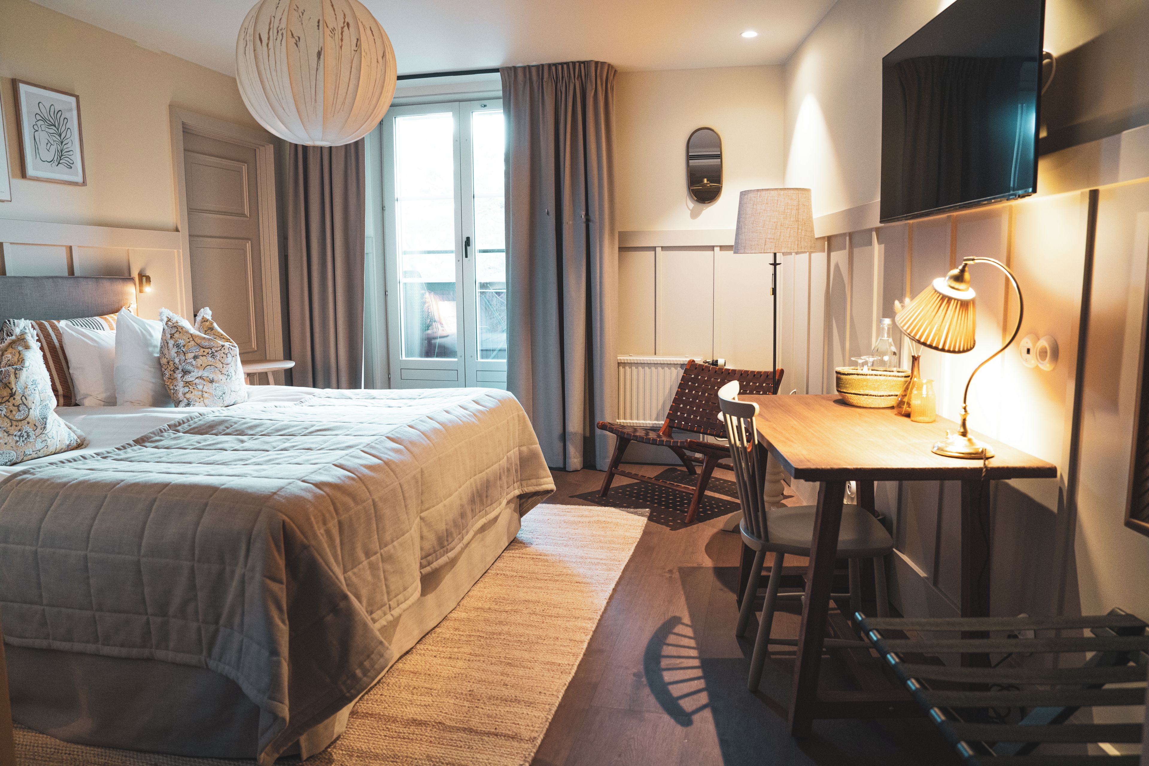 Une chambre d’hôtel équipée d’un lit, d’un bureau, d’une chaise, d’une lampe, d’une télévision et d’une fenêtre avec des rideaux.