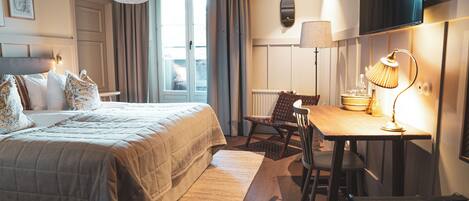 Habitación de hotel con cama, escritorio, silla, lámpara, televisor y ventana con cortinas.