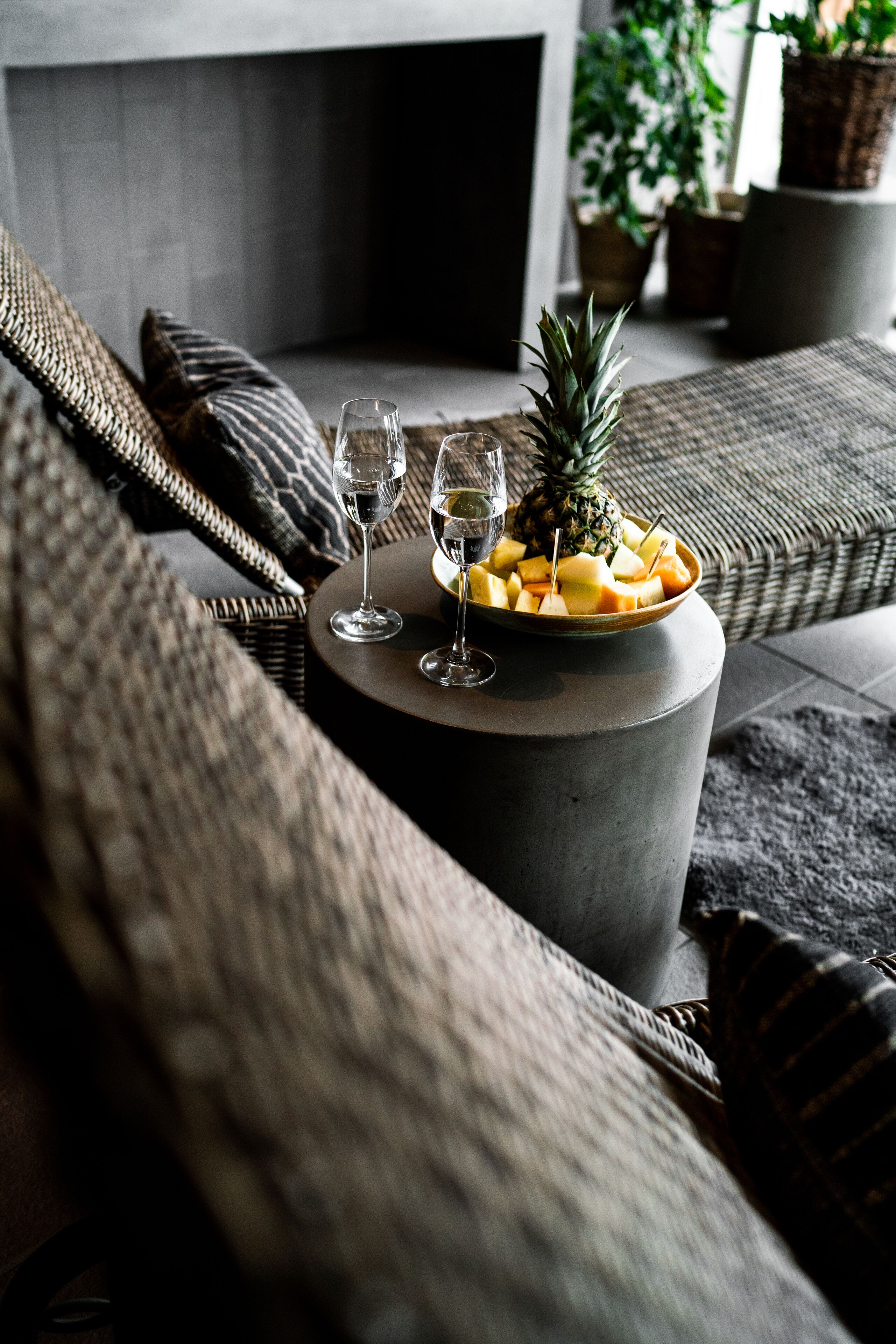 A modern living room with a round coffee table, two wine glasses, a pineapple, and a bowl of fruit.