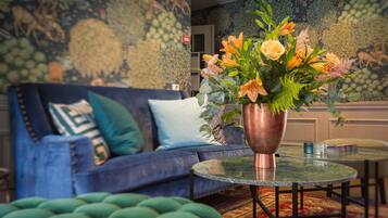 A living room with a blue sofa, green ottoman, and a table with a copper vase of flowers.