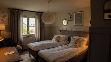 A hotel room with two beds, a desk, a chair, a window with curtains, and wall art.