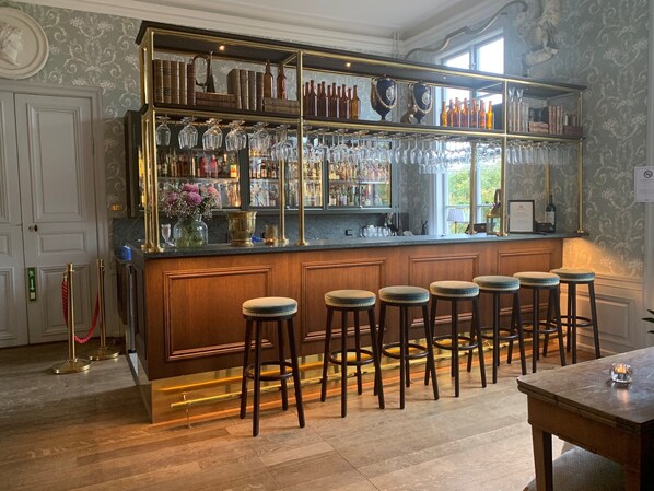 A bar area with a wooden bar counter, multiple stools, and a glass display case containing bottles and glasses. - Krusenberg Herrgård (Knivsta)